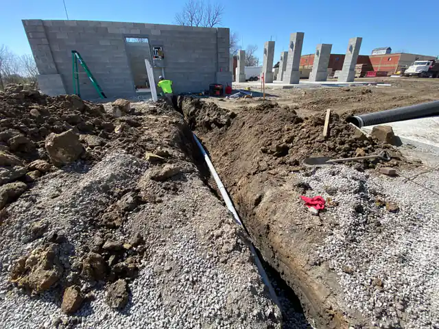 A trench and conduit run at a CMU shell under construction, panel already hung