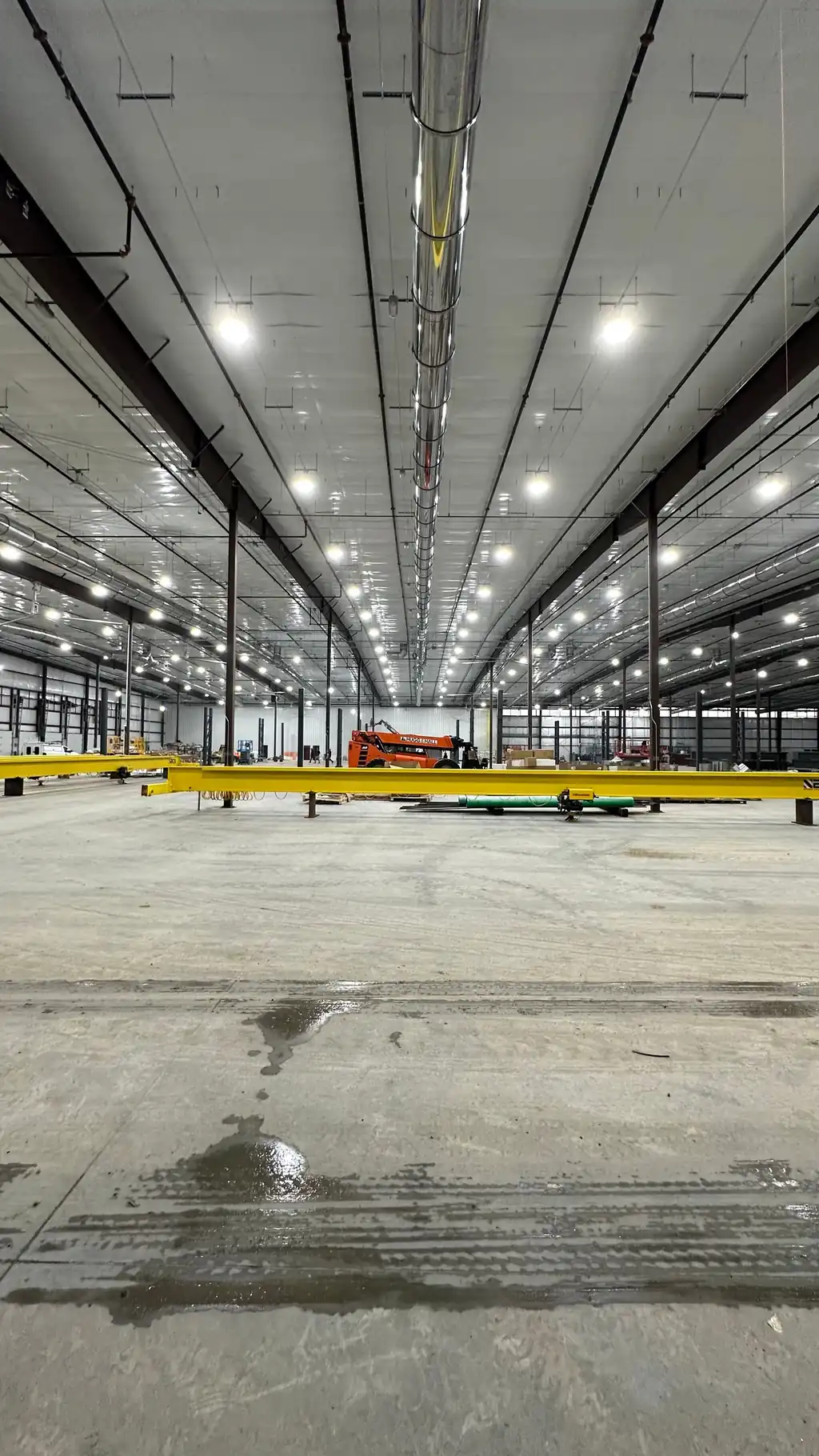 A new distribution center lit end to end, crane rail overhead and a telehandler on the slab