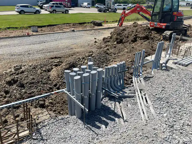 A capped conduit stub-up bundle strapped to strut with an excavator working the trench behind