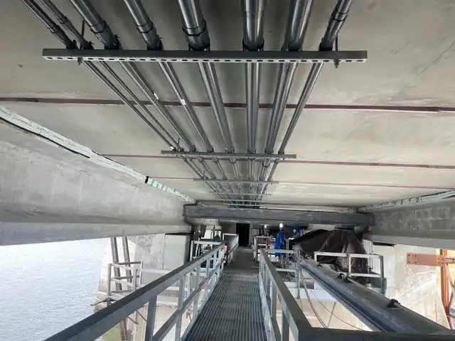 Rigid conduit racked under the spillway bridge deck, walkway running out over open water
