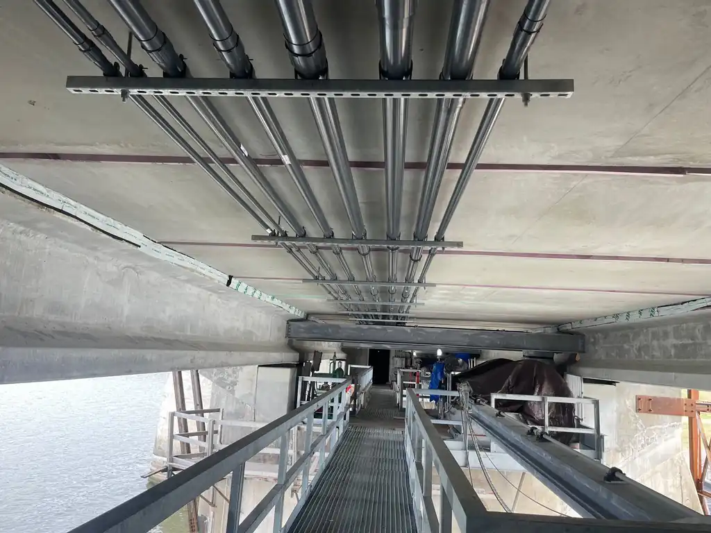 Rigid conduit racked to the underside of a spillway bridge deck above open water
