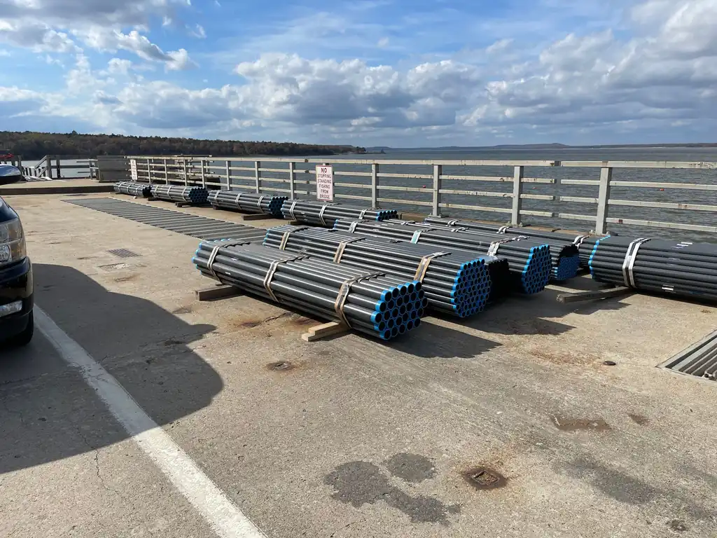 Bundled conduit staged on a dam bridge deck with the lake and treeline behind