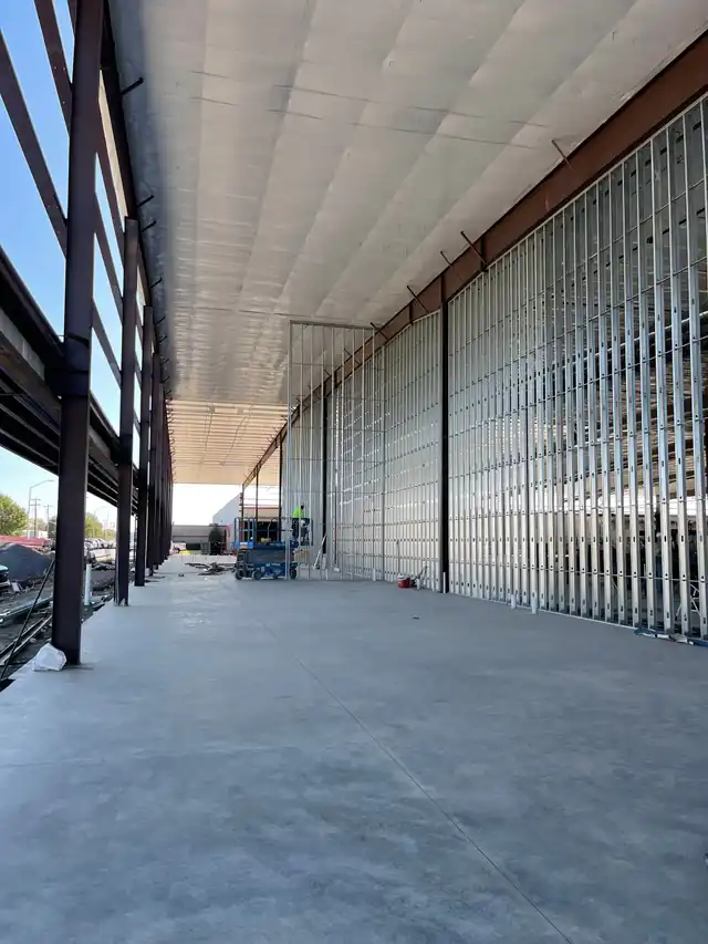 A steel-and-stud building shell under construction with a scissor lift and insulation deck