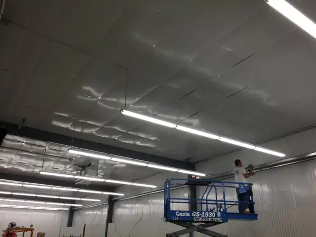 A technician on a scissor lift fixing a high-bay lighting run to the deck