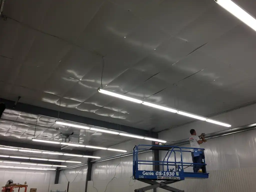 A technician on a scissor lift fixing a high bay lighting run to a warehouse deck